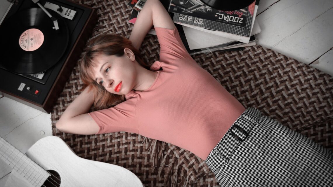 A woman lies on a woven rug, lost in music memories, beside a turntable and a stack of vinyl records